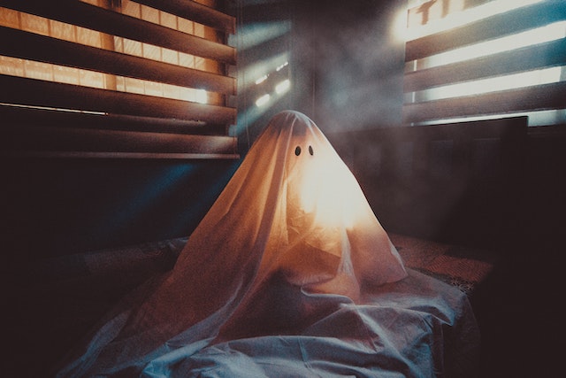A person dressed as a ghost sitting on a bed