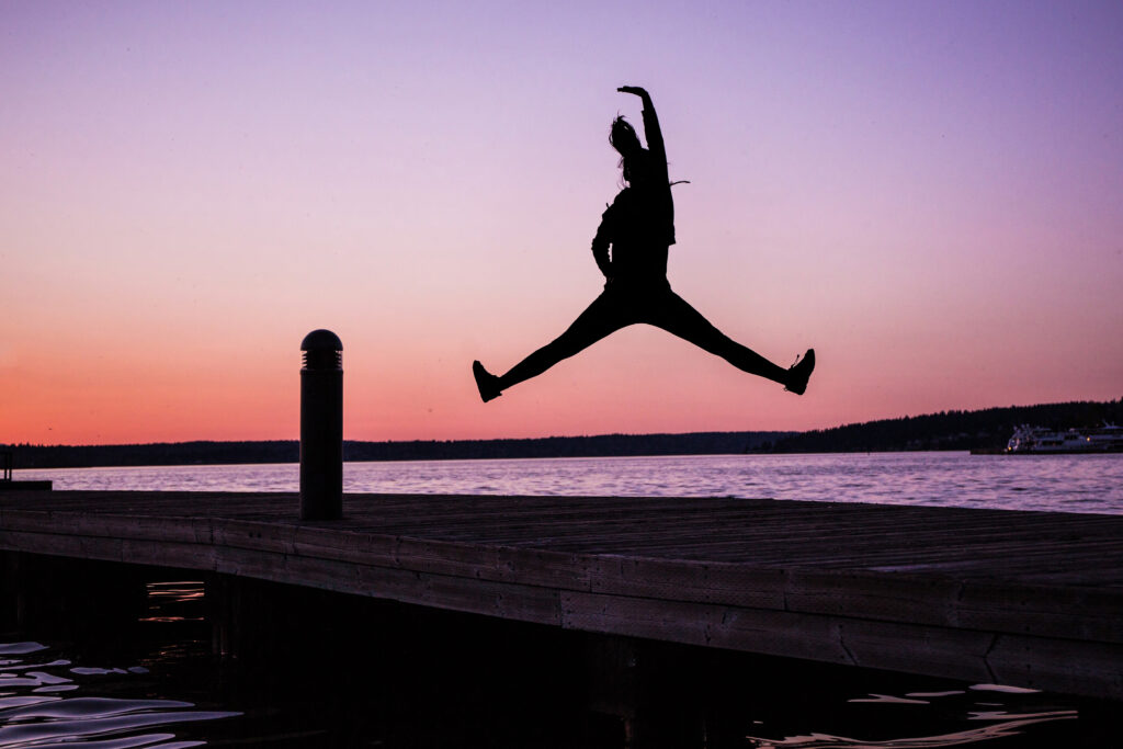 A woman jumping on a beach on a sunset. Purple sky and sea, she's in a shadow.(Do you prefer your favorite song to make you jump and dance, or contemplate?)