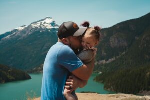 A father holding and kissing his little daughter in front of a river and mountains. (Serbian teacher says, "Ovaj čovek je sjajan tata!")