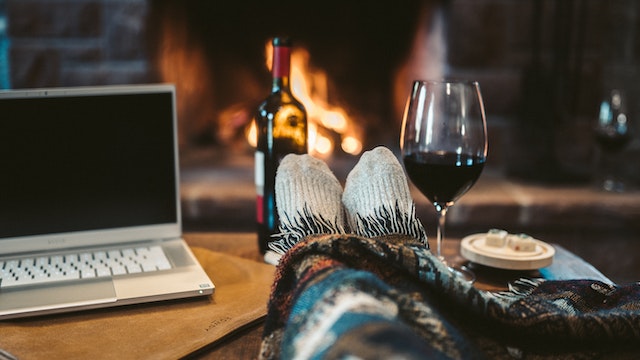 A laptop, a bottle, and a glass of wine, and feet in cosy socks and blanket on the table.(Who says online dates can't be as romantic as live ones?)