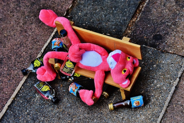 Pink Panther toy laying on a mini-bench with little alcohol bottles around him. It seems drunk.(Learning Serbian Language's idioms: Oh, no! Pink Panther is pijan kao majka!)