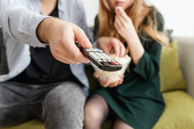A man and a woman sitting on a couch. He's holding a remote and she's holding a bowl of popcorn.
(Learning Serbian with popcorn: prepare yourself for a lot of laughter!)