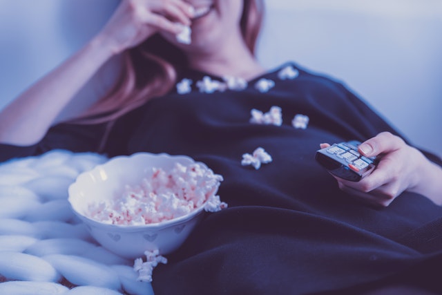 A girl is smiling and eating popcorn while holding a remote and a bowl of popcorn.
(Watching Serbian movies is a perfect way to explore the Serbian language!)