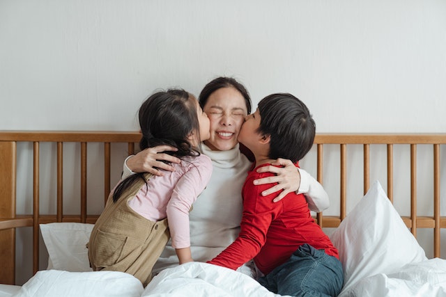 A boy and a girl kissing their mom on both cheeks at the same time. They're sitting in a bed.
Learning Serbian: How would you say "Kiss me"?)
