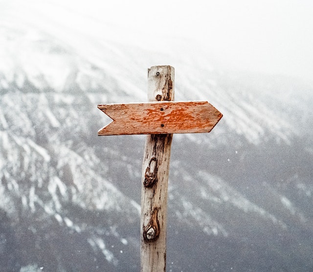 A wooden sign of the direction in front of mountains.