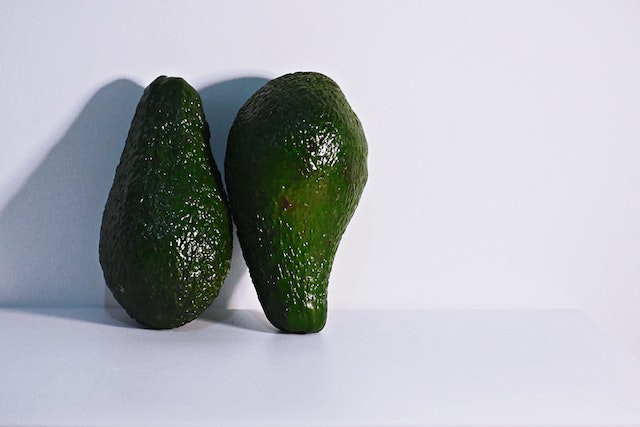 Two avocados standing upside-down next to each other on the white surface.