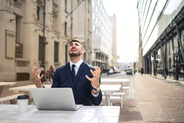 A man is sitting on a bench in a town. A laptop is in front of him and a coffee-to-go is next to him. He's frustrated and looks to the sky like he's asking "Why me?!"
(Don't get too frustrated, there are other ways of learning Serbian!)