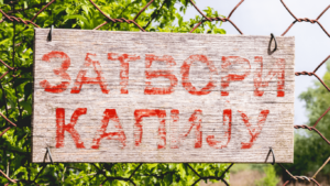 A plank on a fence with the red caption "Zatvori kapiju" written in the Serbian Cyrillic alphabet. It means "Close the gate."
