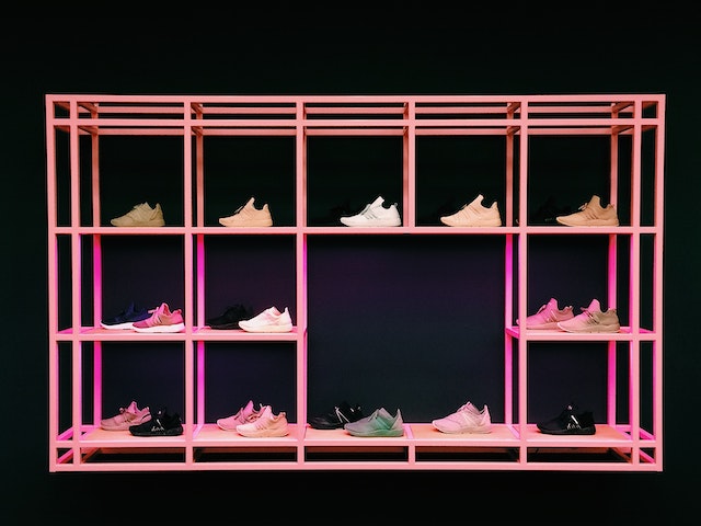 A pink shelf with sneakers on it, with a black background.