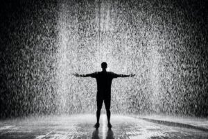 A black and white picture of a man standing in heavy rain with his arms spread.