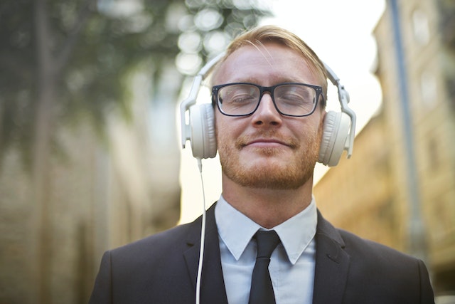 A blonde man with a beard wearing a suit and listening to music through his headphones and smiling (maybe he's listening to Serbian lessons for beginners).