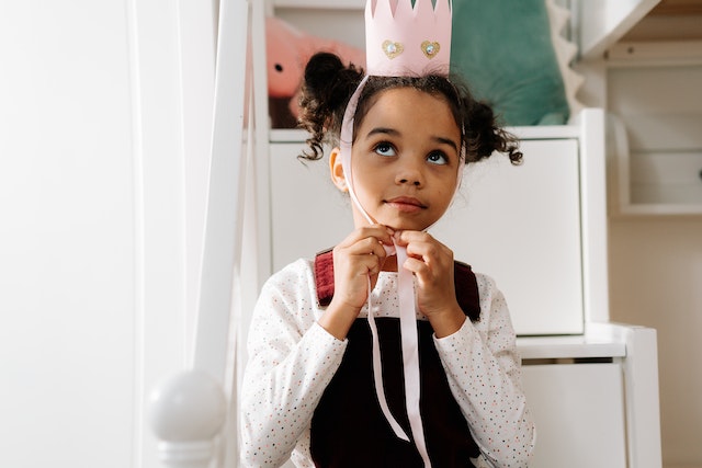 A little girl putting a pink paper crown on her head.
(Ma ti si car(ica) is an expression you won't find in textbook's Serbian lessons for foreigners!)