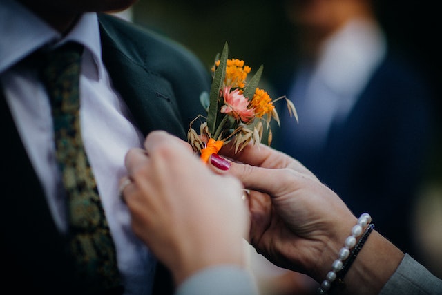 A bride attaching an orange corsage to the groom's jacket.
