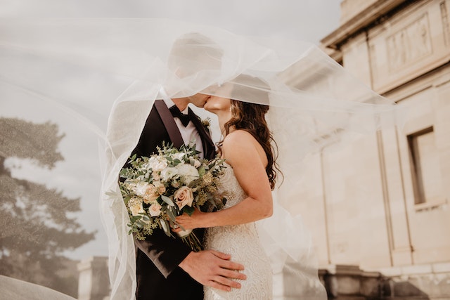 A bride and groom kissing. Her veil is flying in the wind and she's holding a bouquet.
(You can expect some unexpected moments at a Serbian wedding!)
