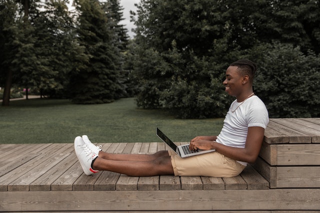 A smiling man sitting in nature on a wooden path, wearing a white T-shirt, white sneakers and beige shorts. He's looking at his laptop.
(Are Serbian private lessons the right choice for you?)