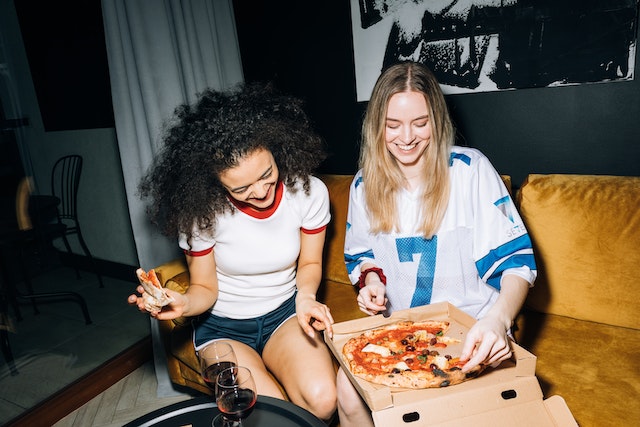 Two girls sitting on a couch and eating pizza. They're dressed casual and smiling.
(Serbian cases made easy: try saying, "I'm eating pizza with my friend" in Serbian!)