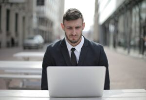 A man in a suit sitting in front of a laptop with a worried look on his face.