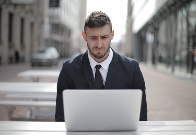 A man in a suit sitting in front of his laptop with a troubled face.
