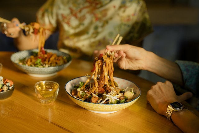 Two people eating Chinese food using chopsticks.