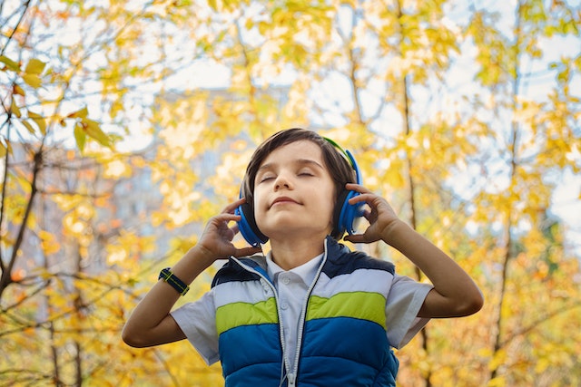 A boy in the woods listening to music through blue headphones, and enjoying.