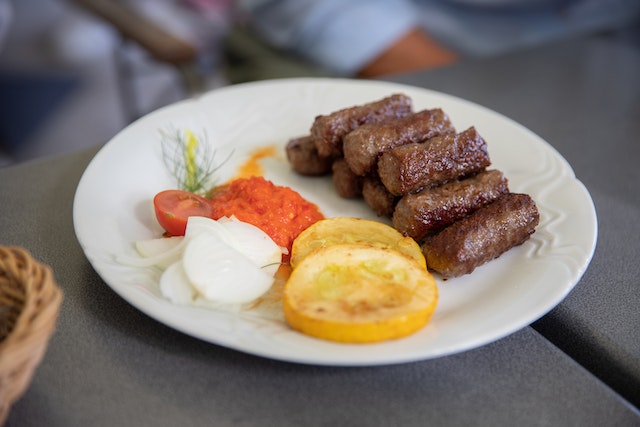 A plate with ćevapi, ajvar, potato, and onion. Learn Serbian eating habits to blend into the culture better!